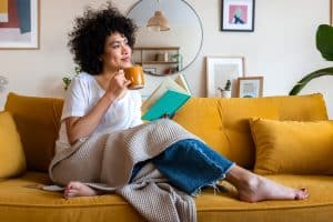 Young woman engaging in self-care with a cup of tea and a book on the couch